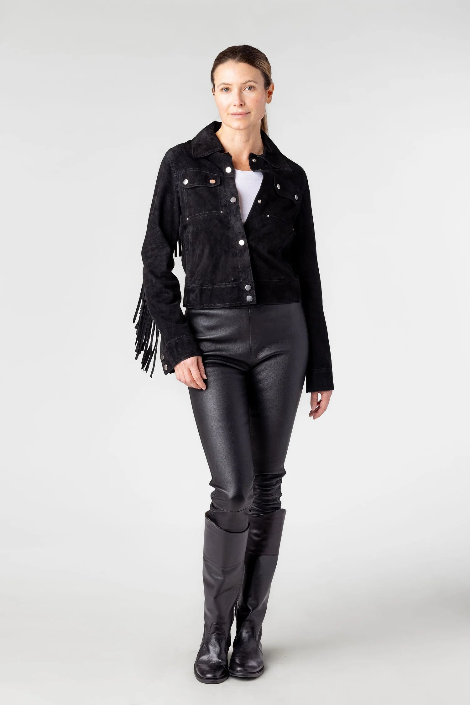 Person wearing a black jacket with fringe details, black leather pants, and black knee-high boots on a white background