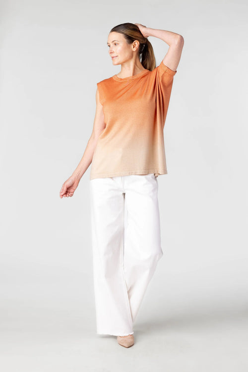 Woman wearing an orange and beige gradient top with white pants on a light gray background