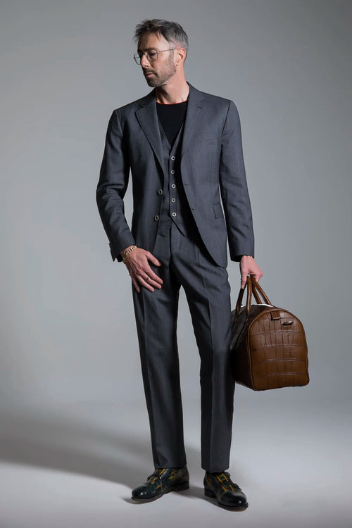 Man in a gray suit holding a brown leather bag against a plain background